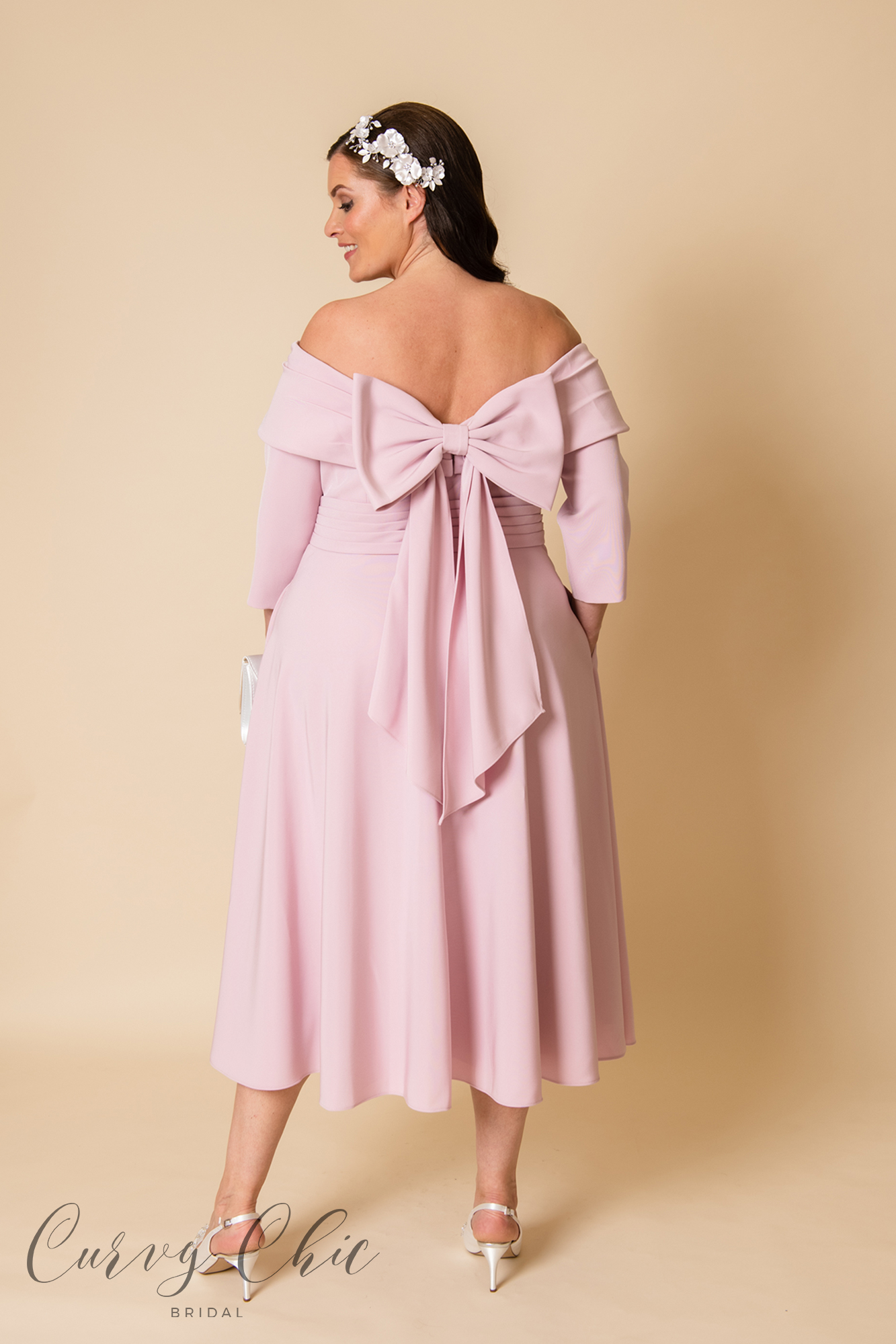 https://www.curvychicbridal.com/app/uploads/2022/09/29668c-in-blush-with-pockets-and-bow-detail-plus-size-mother-of-the-groom-midi-dress-back-3.jpg
